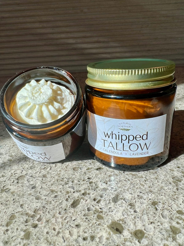 Two jars of Natural Northern's Wisconsin whipped tallow on a concrete surface with a wooden background