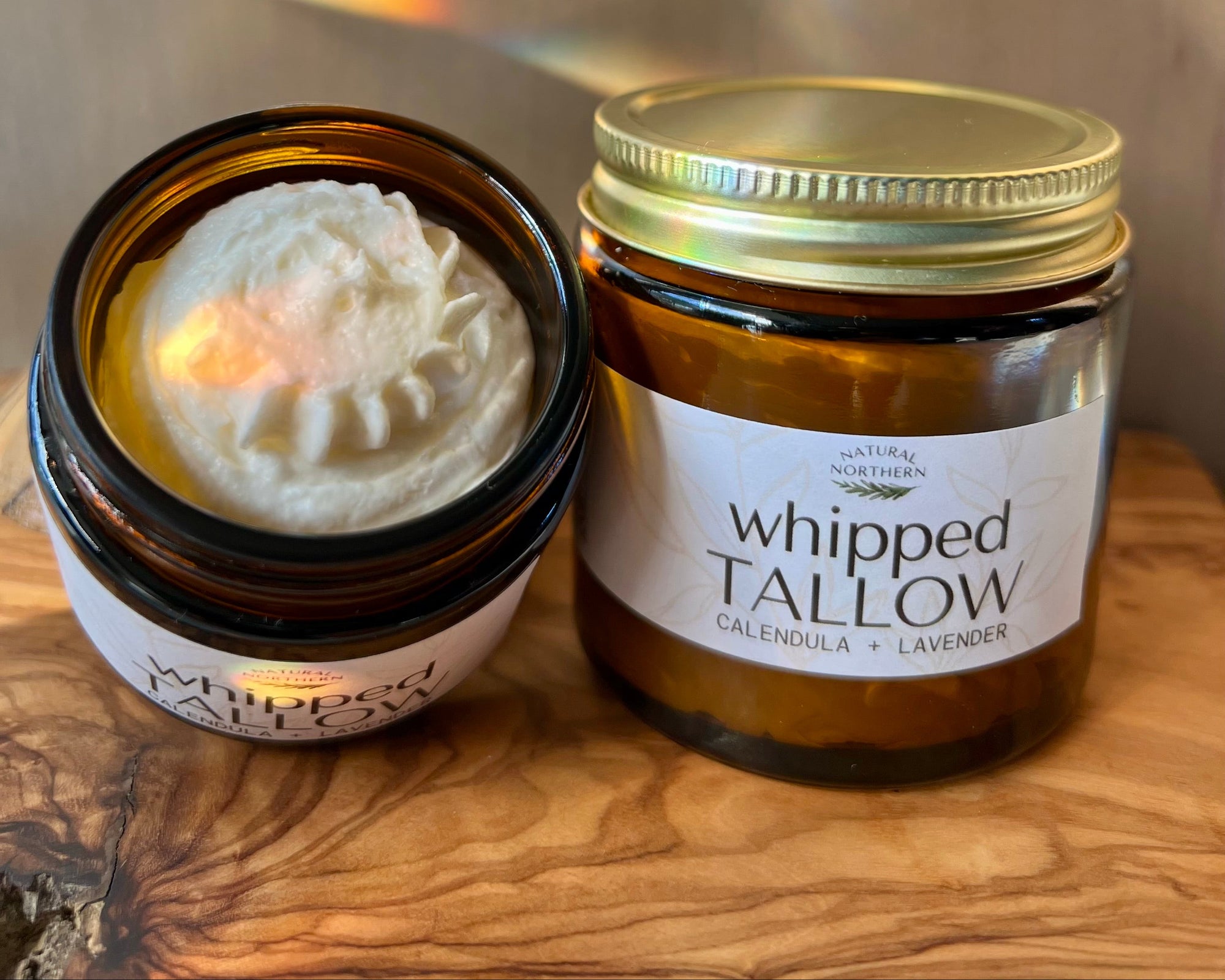 Jar of whipped tallow with a lid on a wooden surface. Organic grass-fed tallow for dry skin, infused with calendula and lavender essential oil for extra skin soothing. great for sensitive skin. 