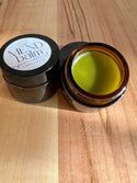 Mend balm jar with lid open on a wooden surface. comfrey infused jojoba oil with tallow balm. 